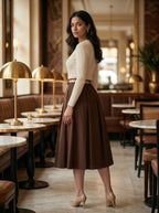 Woman in a brown skirt and white top standing in a stylish restaurant.
