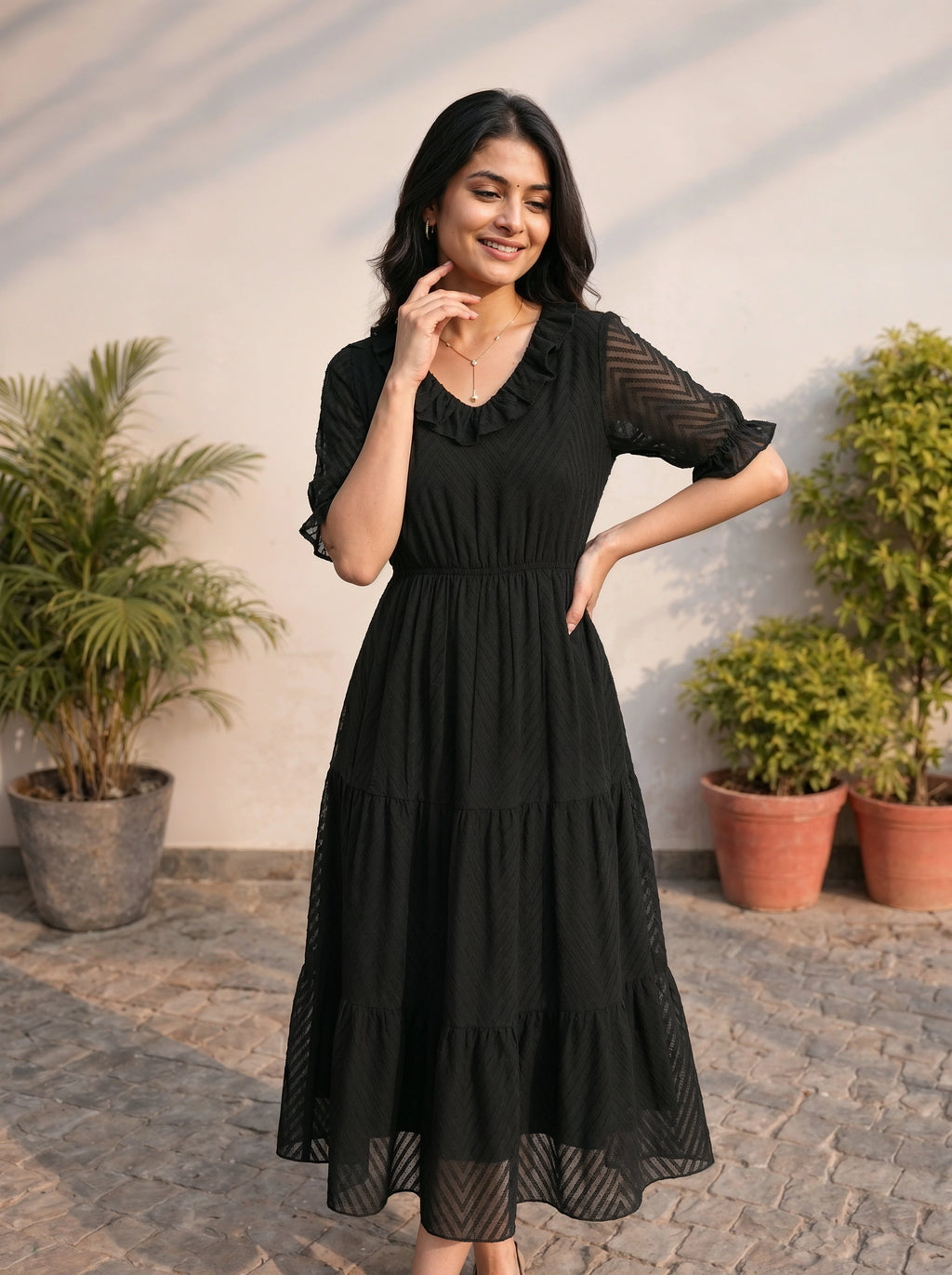Woman wearing a black dress standing outdoors with plants in the background