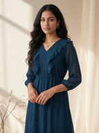 Woman wearing a blue dress with ruffled details against a neutral background