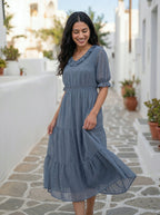 Woman in a blue dress standing on a stone path with plants and white walls in the background