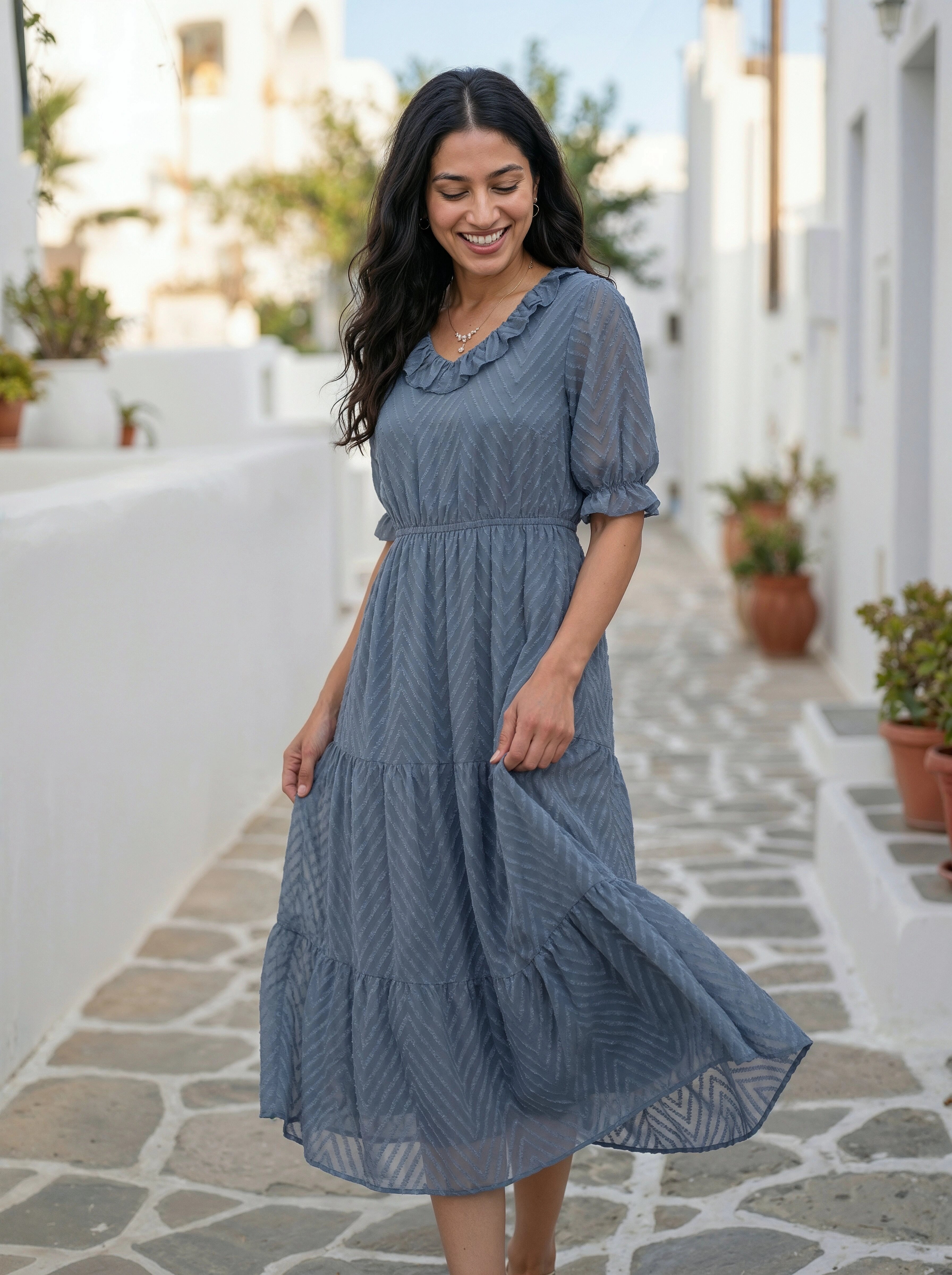 Woman in a blue dress standing on a stone path with plants and white walls in the background