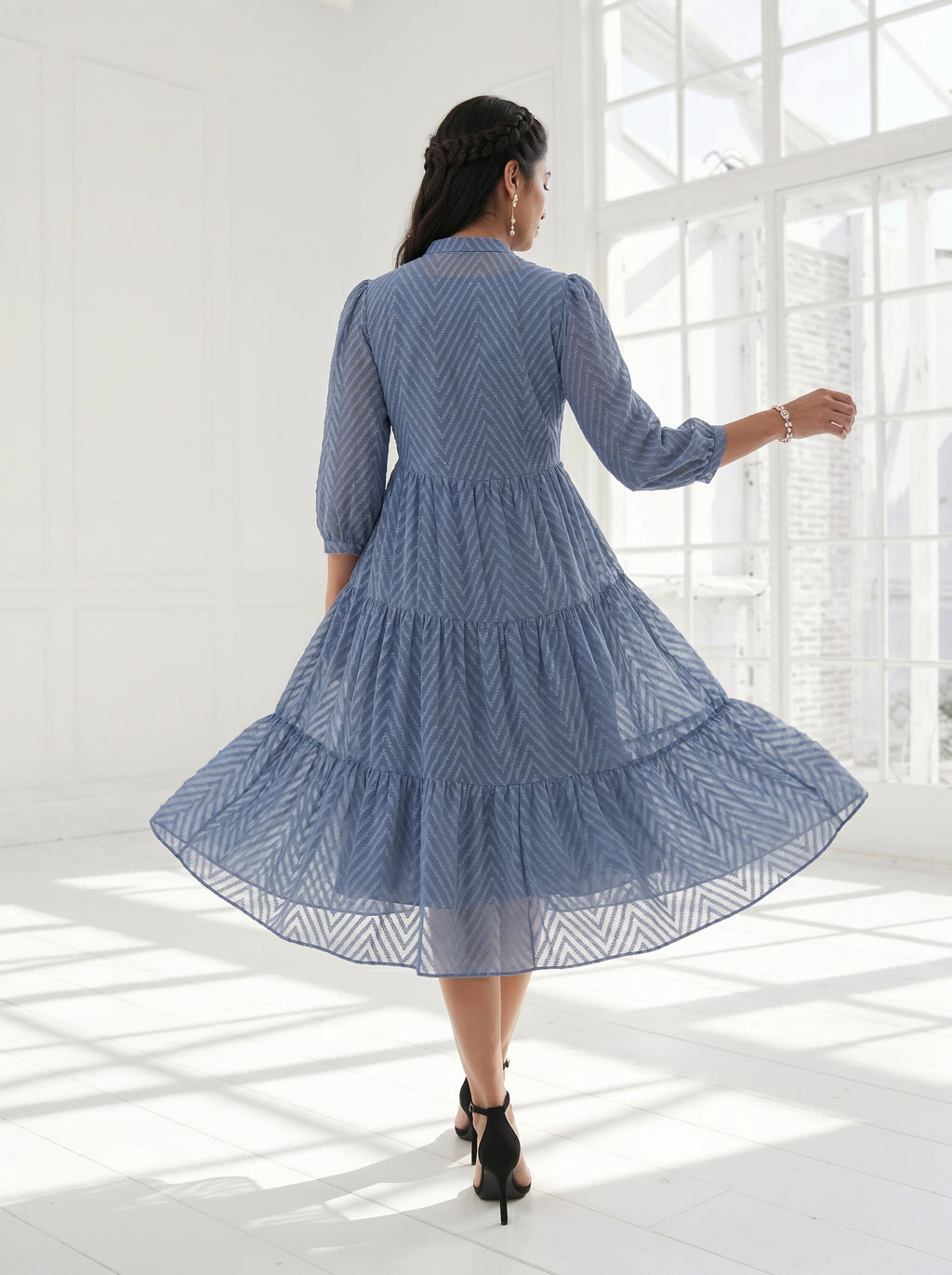 Woman in a blue dress standing in a bright room with large windows.