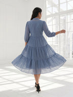 Woman in a blue dress standing in a bright room with large windows.