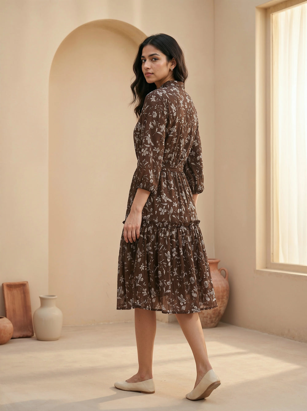 Woman in a floral dress standing in a sunlit room with neutral decor