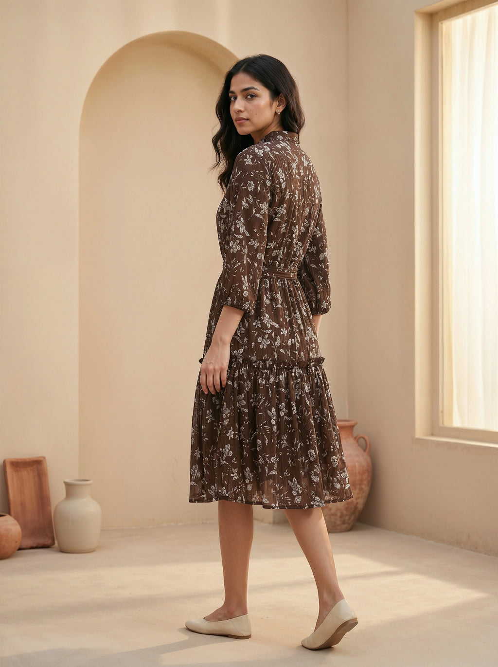 Woman in a floral dress standing in a sunlit room with neutral decor
