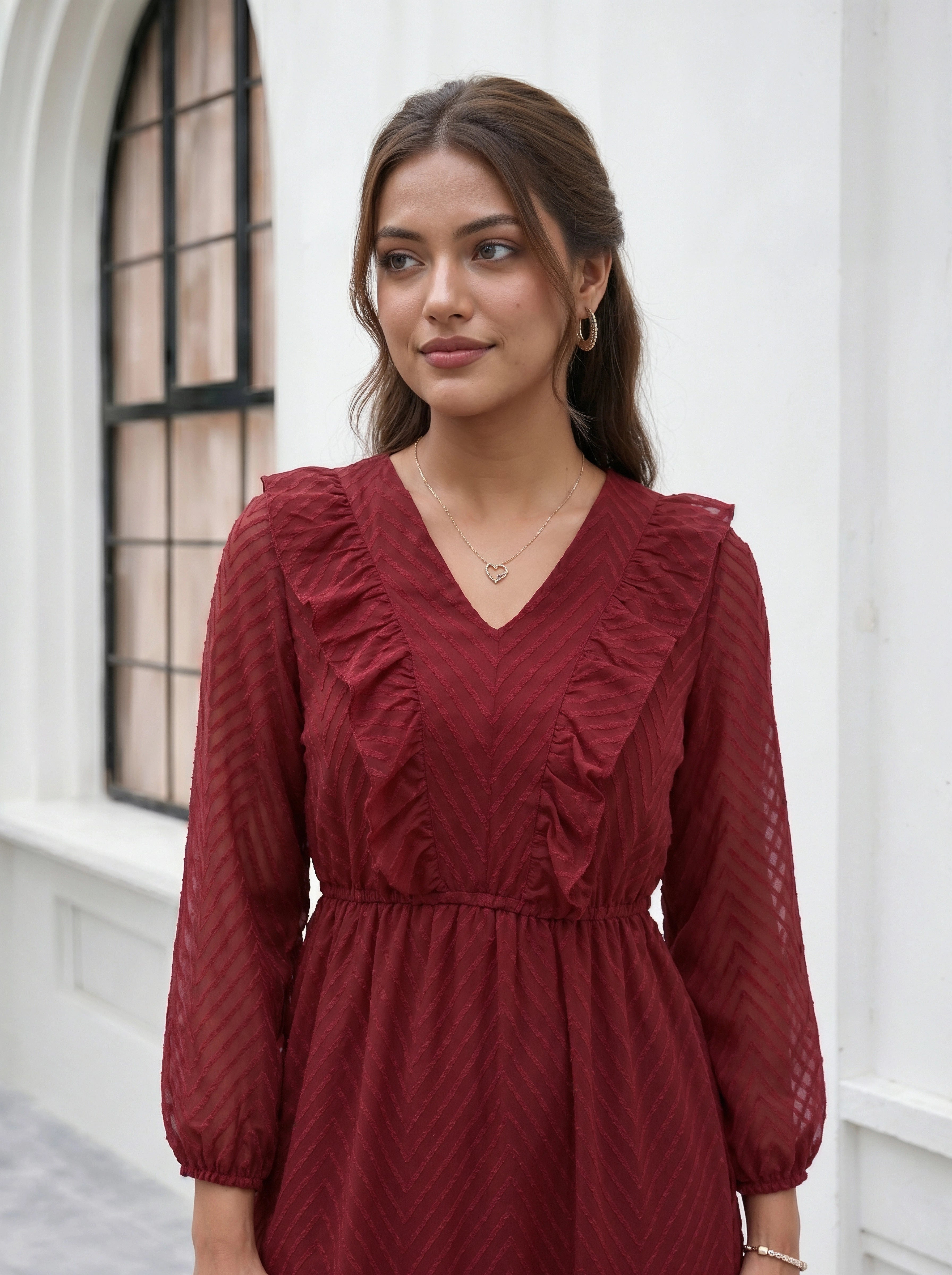 Woman wearing a red dress standing in front of a white wall with a window.