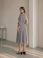 Woman in a patterned dress standing in a minimalistic room.