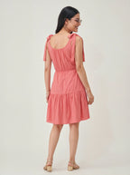 Woman wearing a pink dress with cut-out back design on a white background