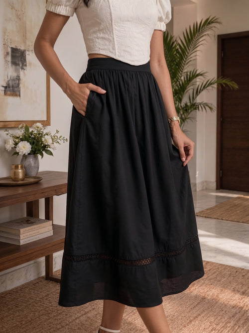 A woman modeling a dusty rose pink tiered midi dress with three-quarter sleeves, a high neck, and a tie-front detail, standing against a white draped fabric backdrop.