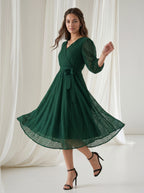 Woman wearing a green dress with a white curtain background