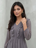 Woman wearing a gray dress with ruffled details against a neutral background
