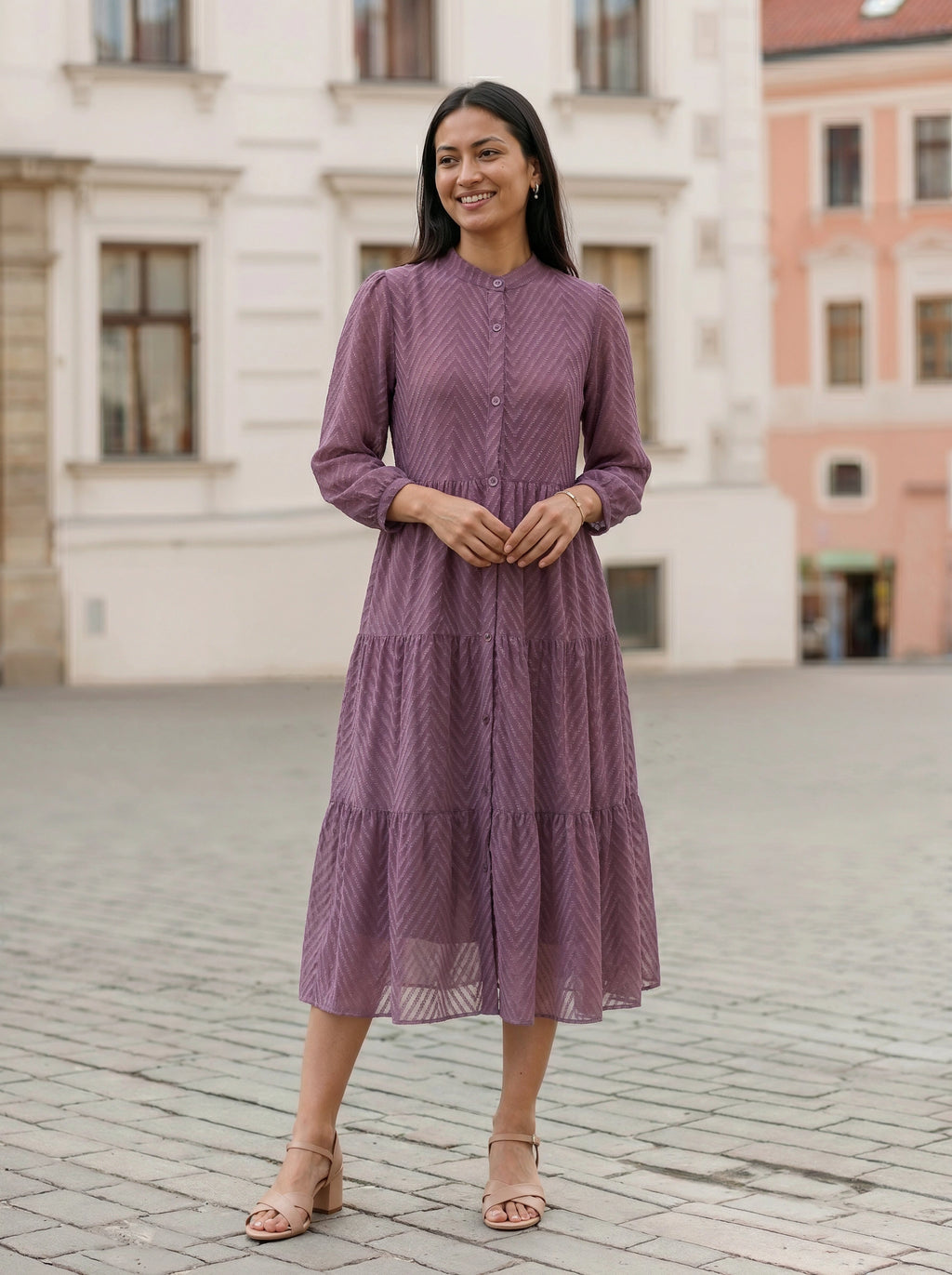 Woman in a purple dress standing on a cobblestone street with buildings in the background