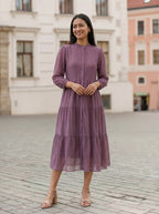Woman in a purple dress standing on a cobblestone street with buildings in the background