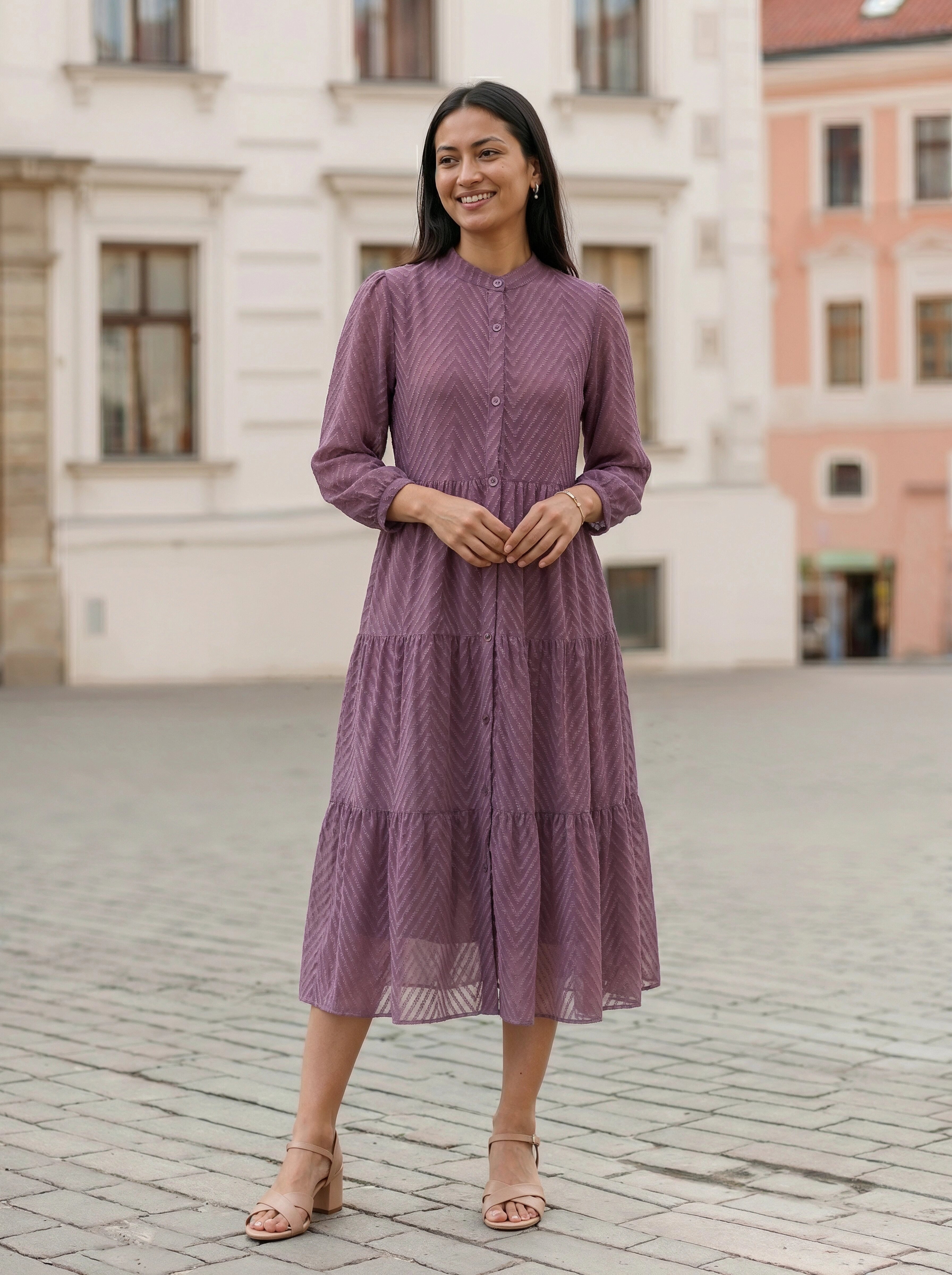 Woman in a purple dress standing on a cobblestone street with buildings in the background