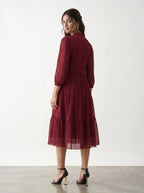 Woman wearing a burgundy dress with long sleeves and a tiered skirt against a white background