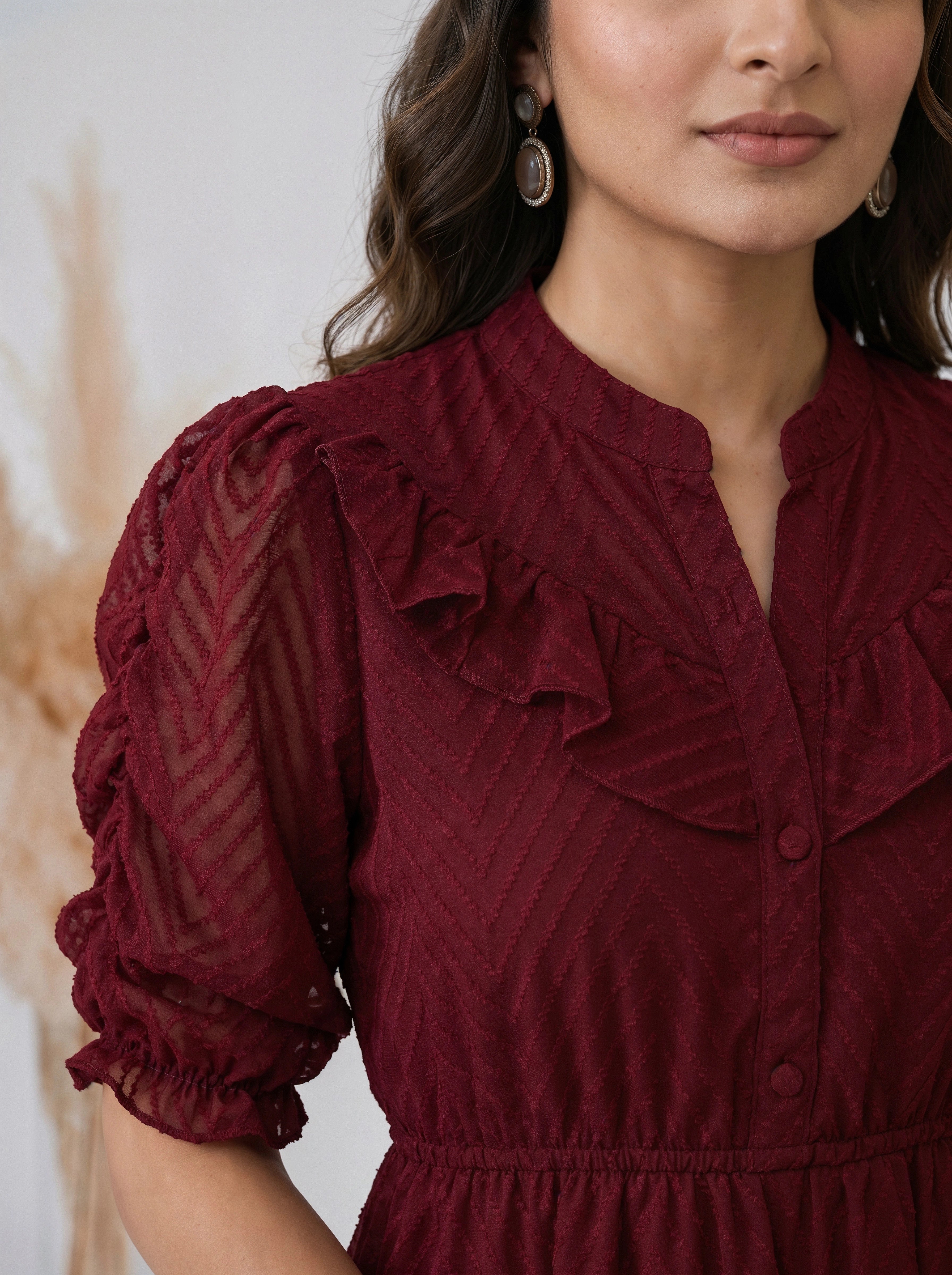 Woman posing in a textured maroon mid length dress with puff sleeves