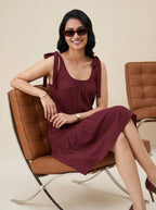 Woman in a burgundy dress sitting on a brown leather chair with a beige background
