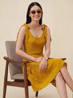 Woman in a yellow dress sitting on a chair against a beige background