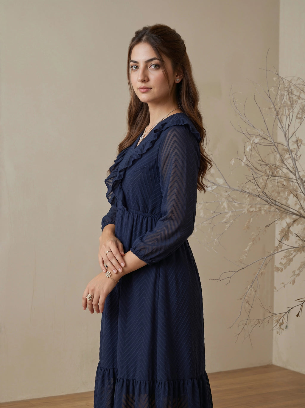 Woman wearing a navy blue dress with ruffled details against a beige wall.