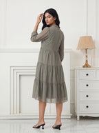Woman in a patterned dress standing in a room with white walls and furniture.