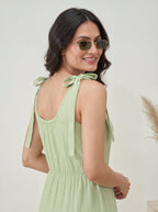 Woman wearing a light green dress with tied sleeves against a plain background