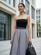 Woman wearing a black strapless top and gray pleated skirt in an urban setting