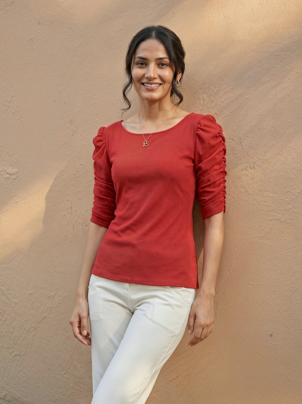 Woman wearing a red top with puffed sleeves against a beige wall
