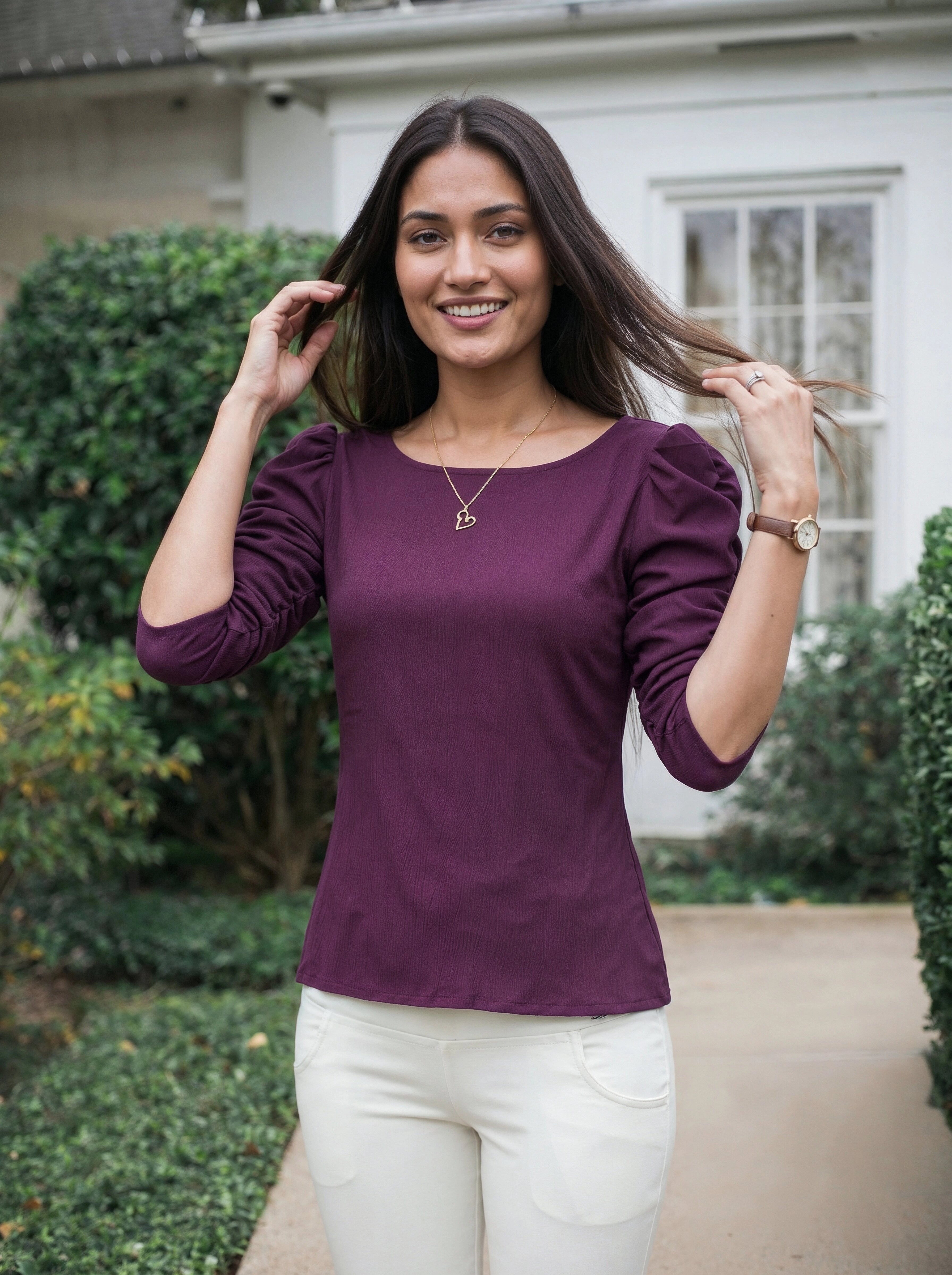Woman wearing a purple top and white pants standing outdoors.