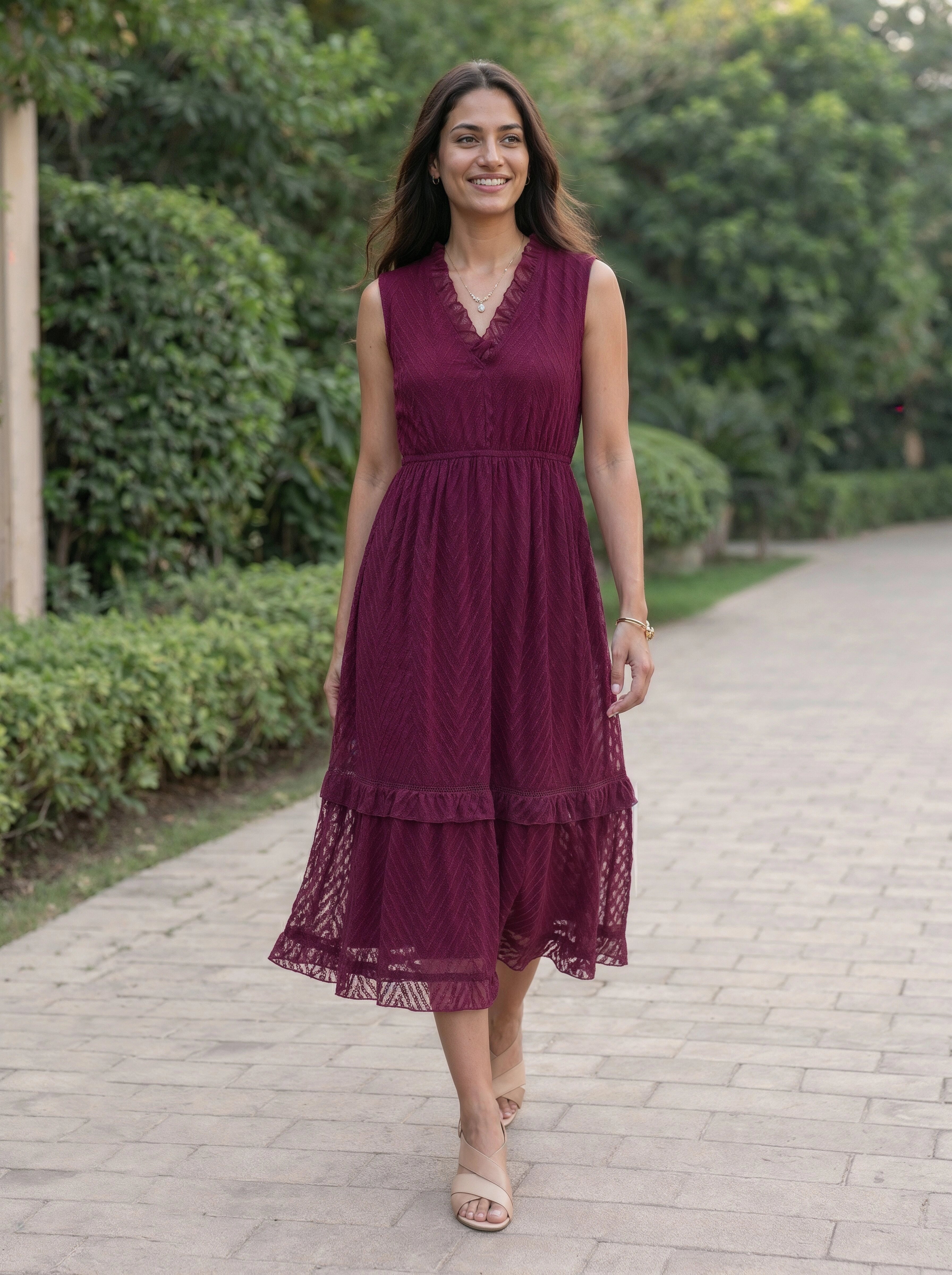Woman in a burgundy dress walking on a path with greenery in the background