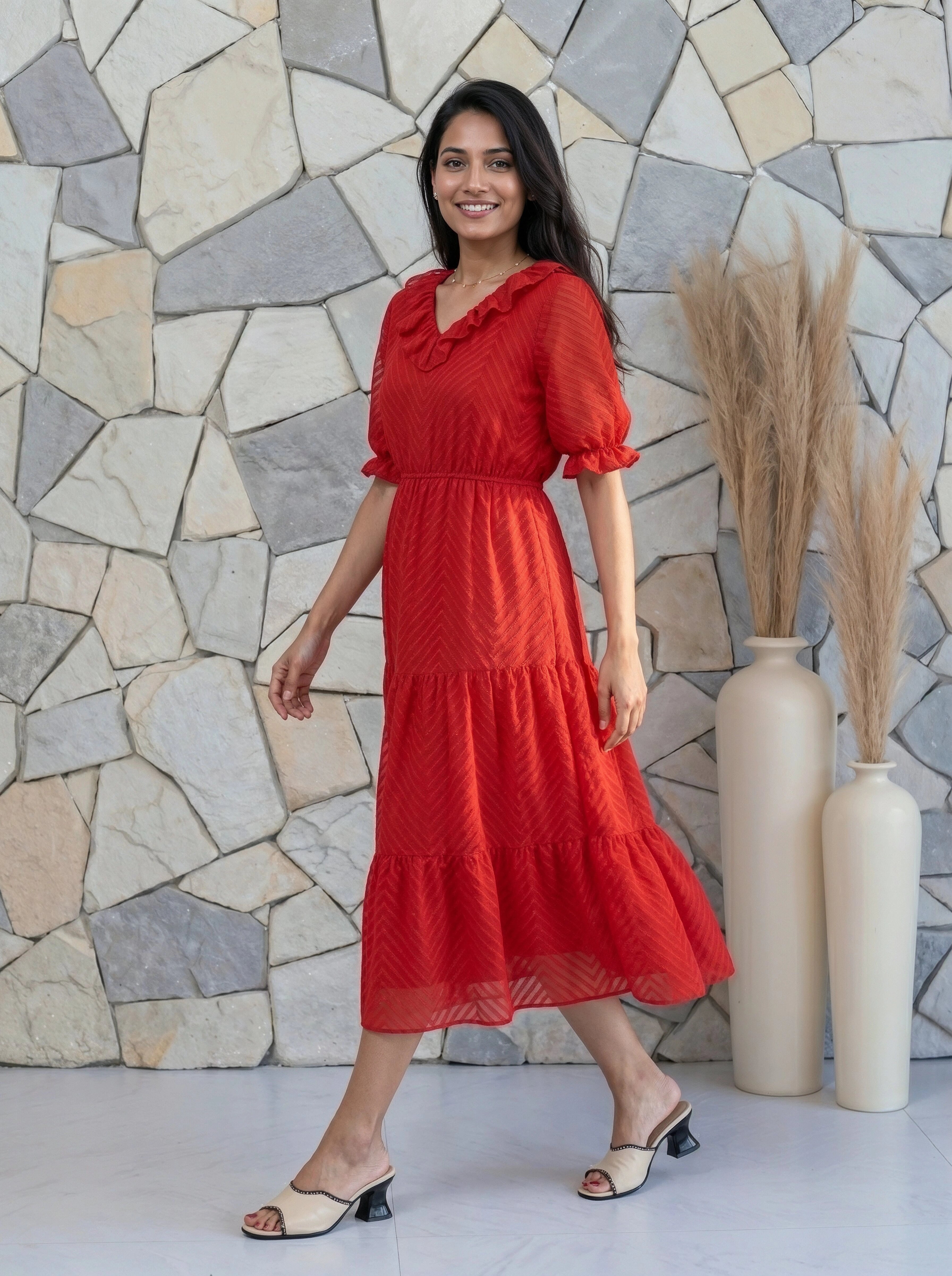 Woman in a red dress standing against a stone wall with decorative vases.