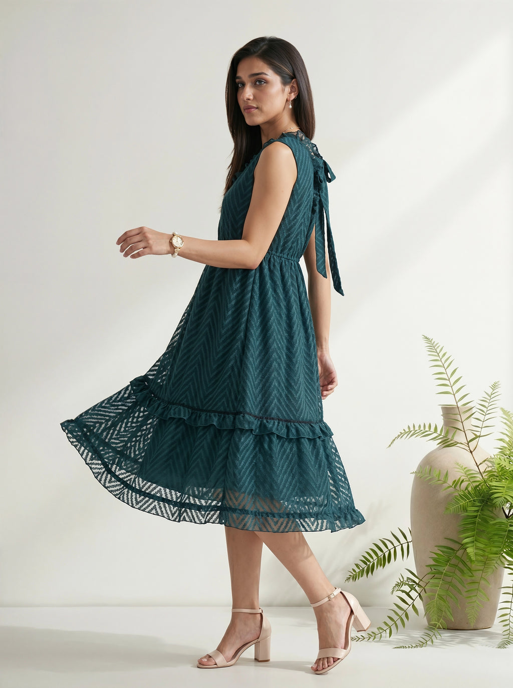 Woman wearing a teal dress with a white background and plant decor