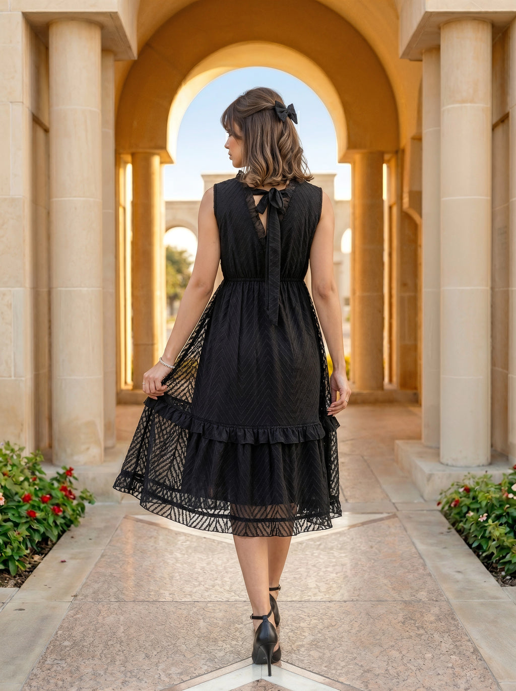 Woman in a black dress standing in an architectural setting with columns and arches.