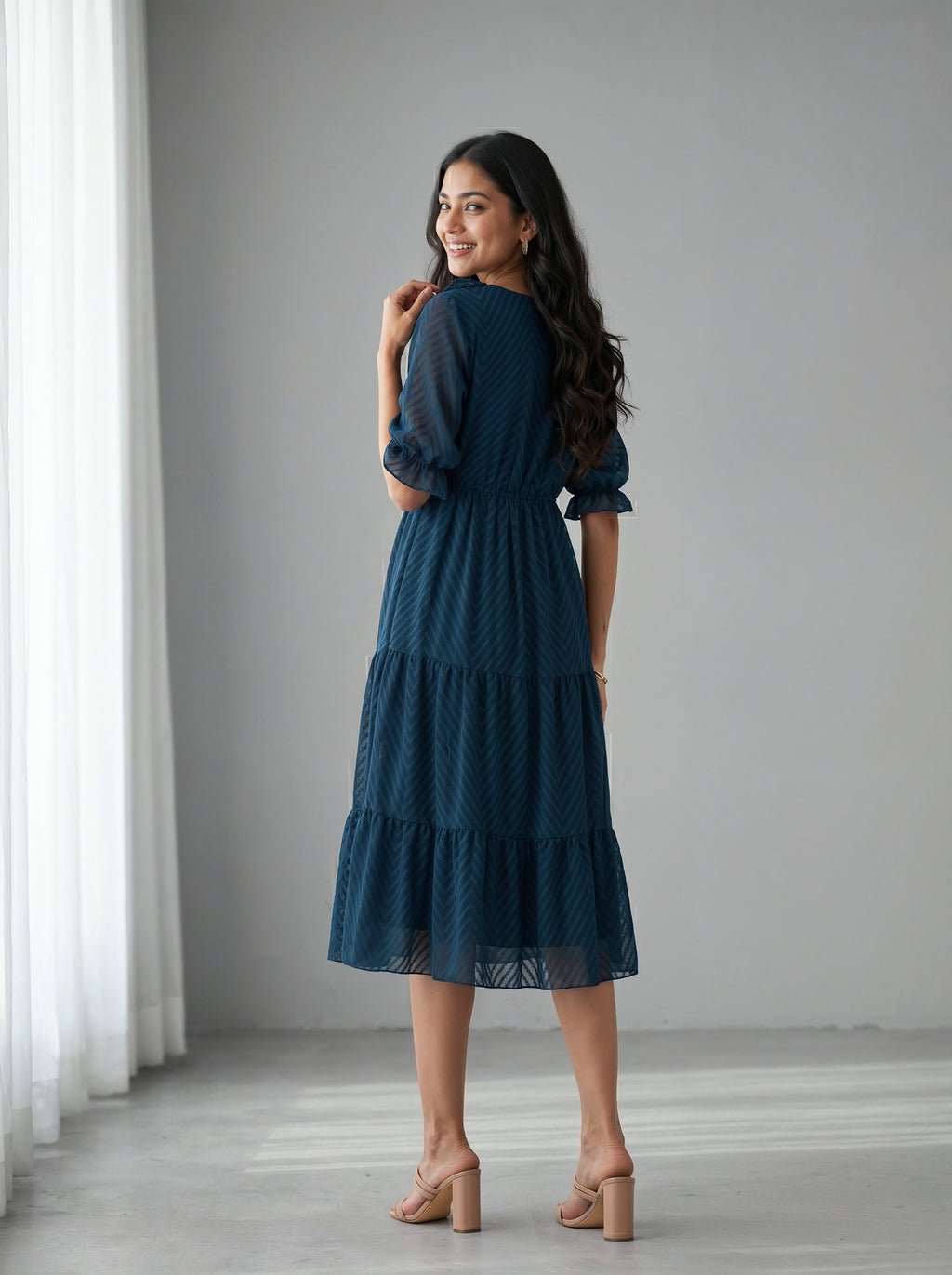 Woman wearing a blue dress standing in a room with white curtains.