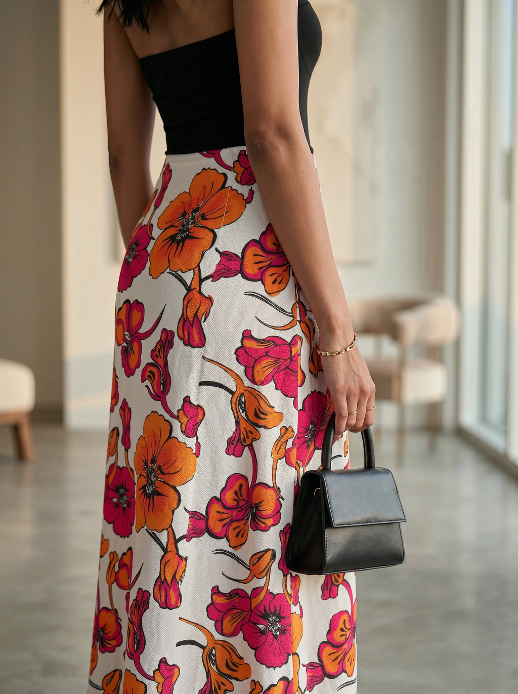 Person wearing a floral skirt with orange and pink flowers on a white background, holding a black handbag.