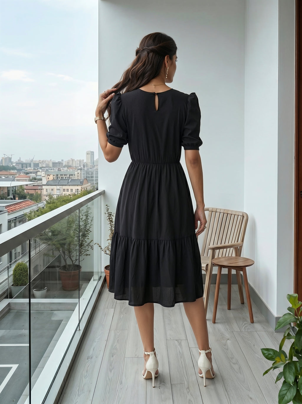 Woman in a black dress standing on a balcony with a cityscape view