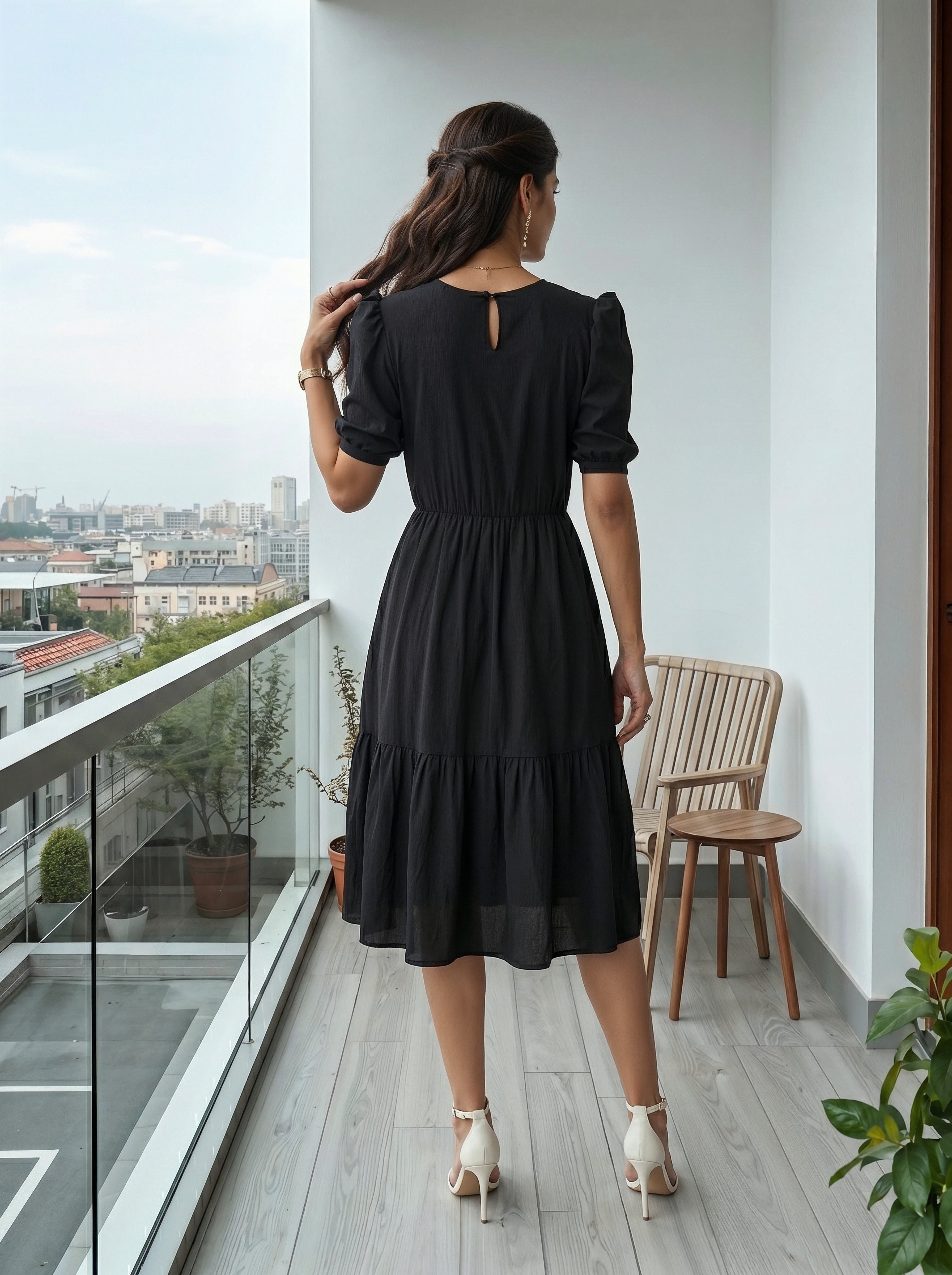 Woman in a black dress standing on a balcony with a cityscape view