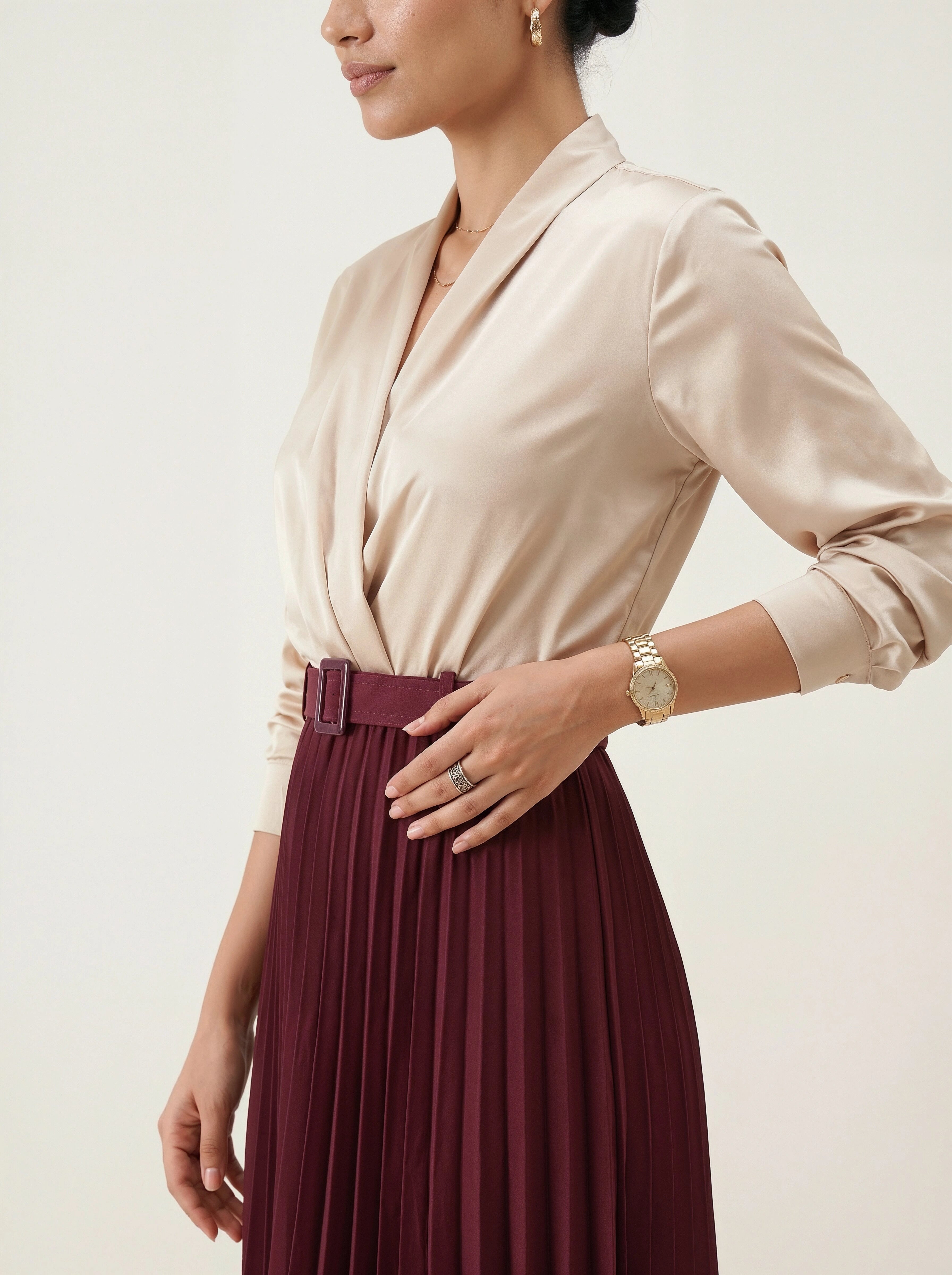 Woman wearing a beige blouse and maroon pleated skirt with a neutral background