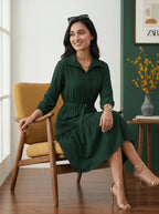 Woman in a green dress sitting on a wooden chair in a bright room.