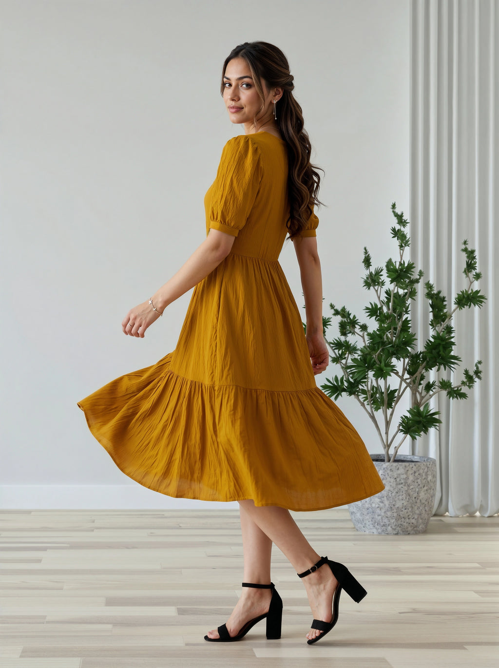 Woman in a mustard yellow dress standing in a room with a plant in the background