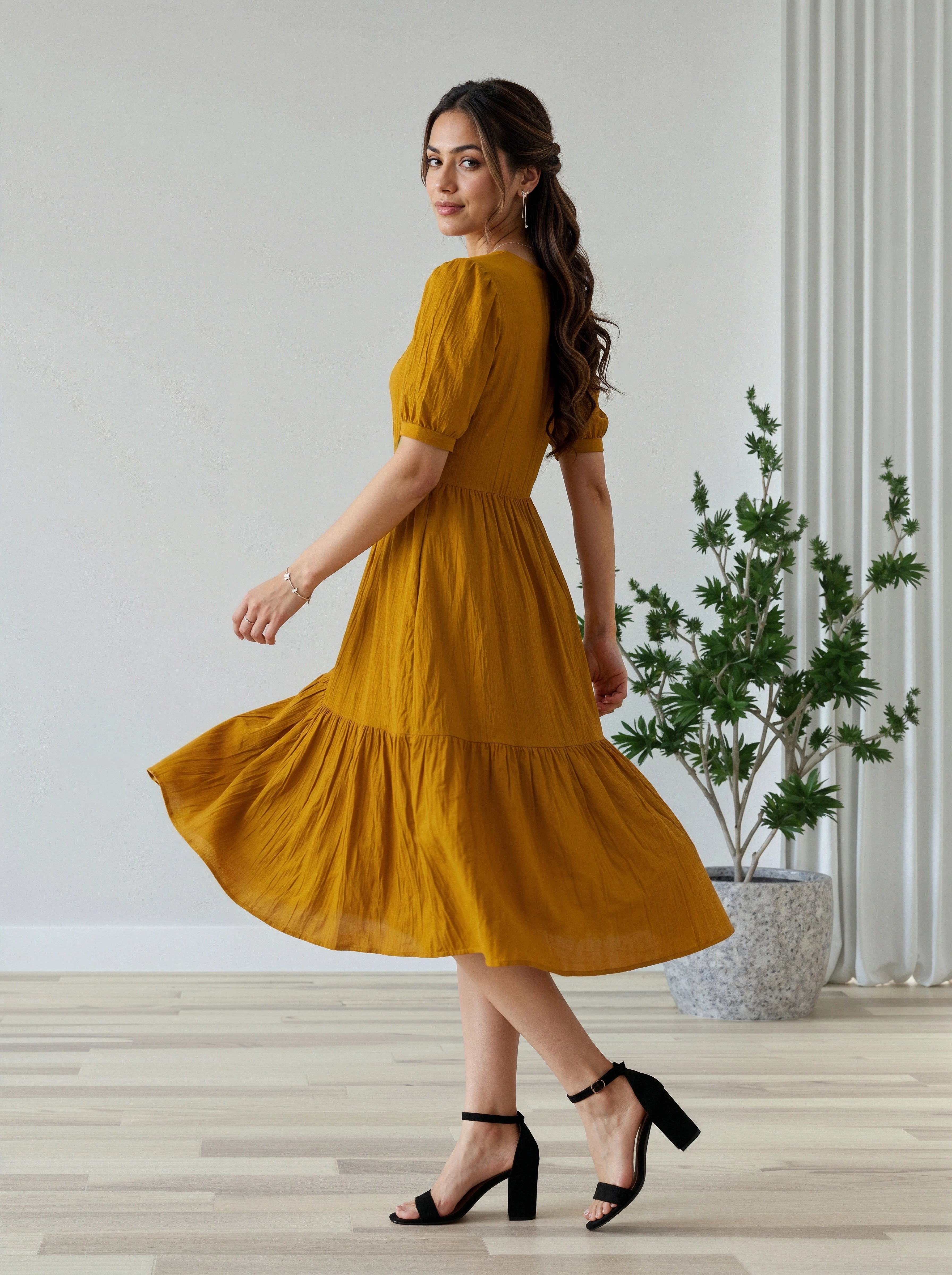 Woman in a mustard yellow dress standing in a room with a plant in the background