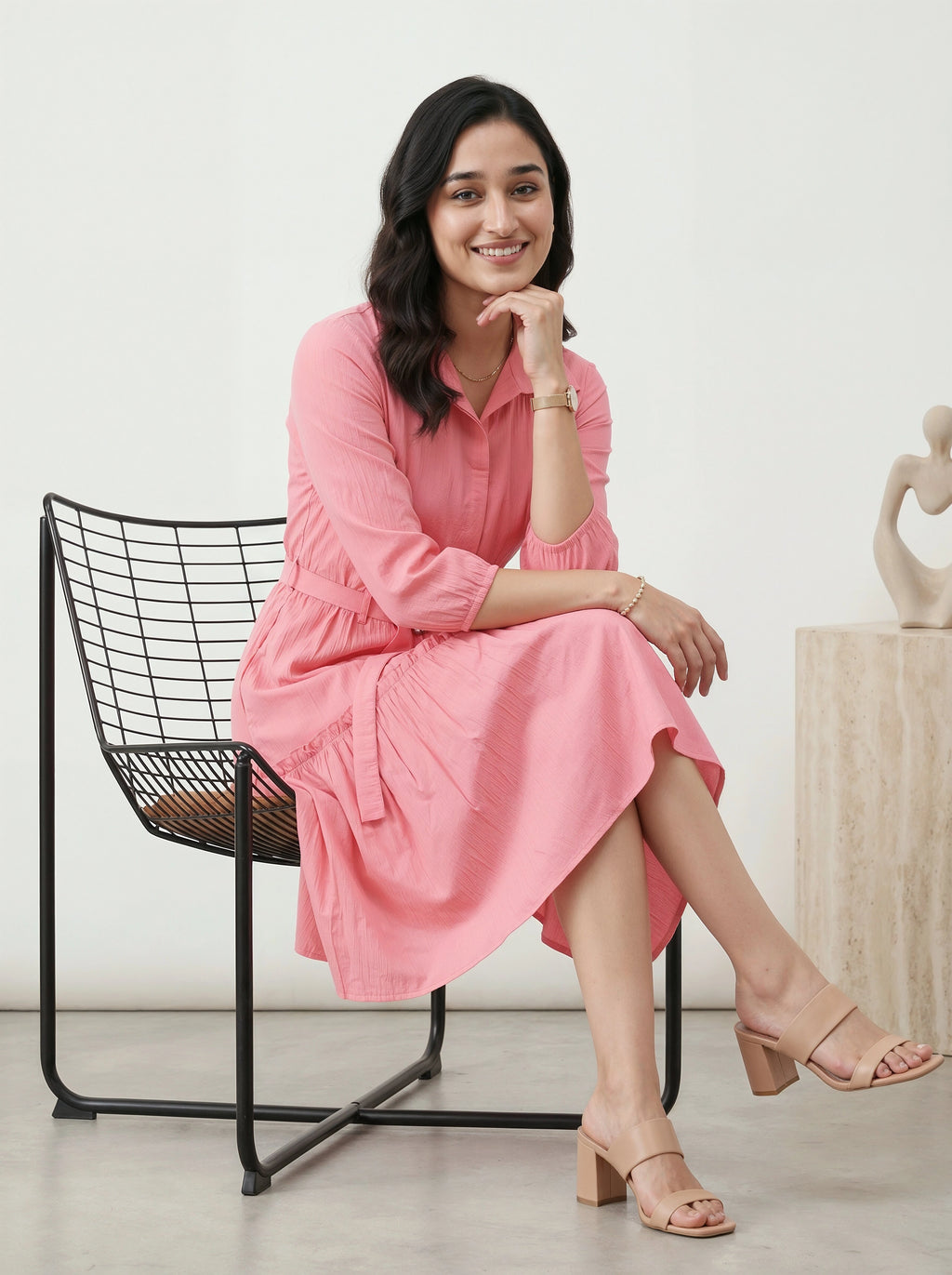 Woman in a pink dress sitting on a black chair with a white background