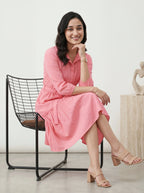 Woman in a pink dress sitting on a black chair with a white background