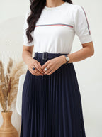 Woman wearing a white top with red and blue stripes and a navy pleated skirt.