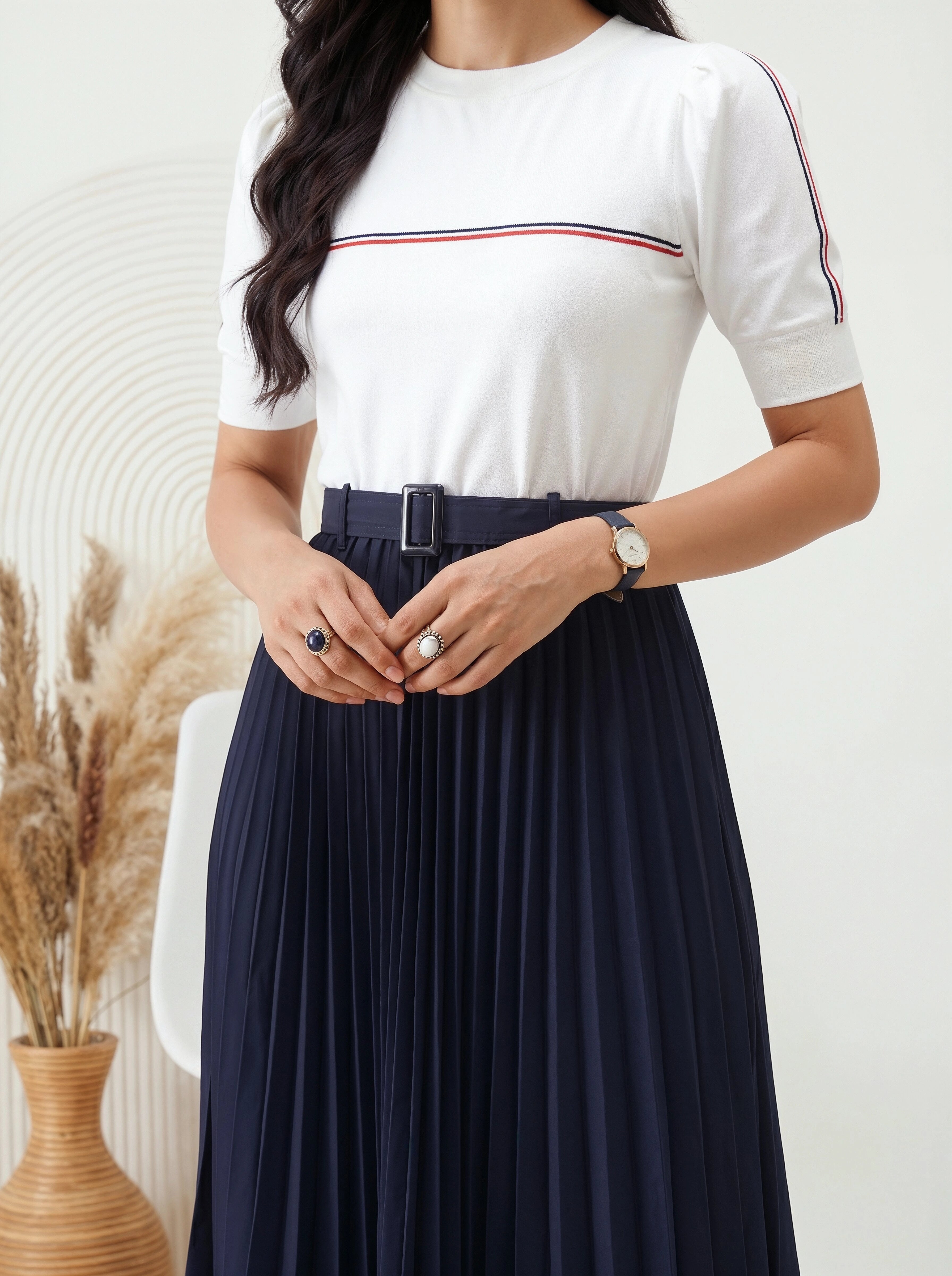 Woman wearing a white top with red and blue stripes and a navy pleated skirt.