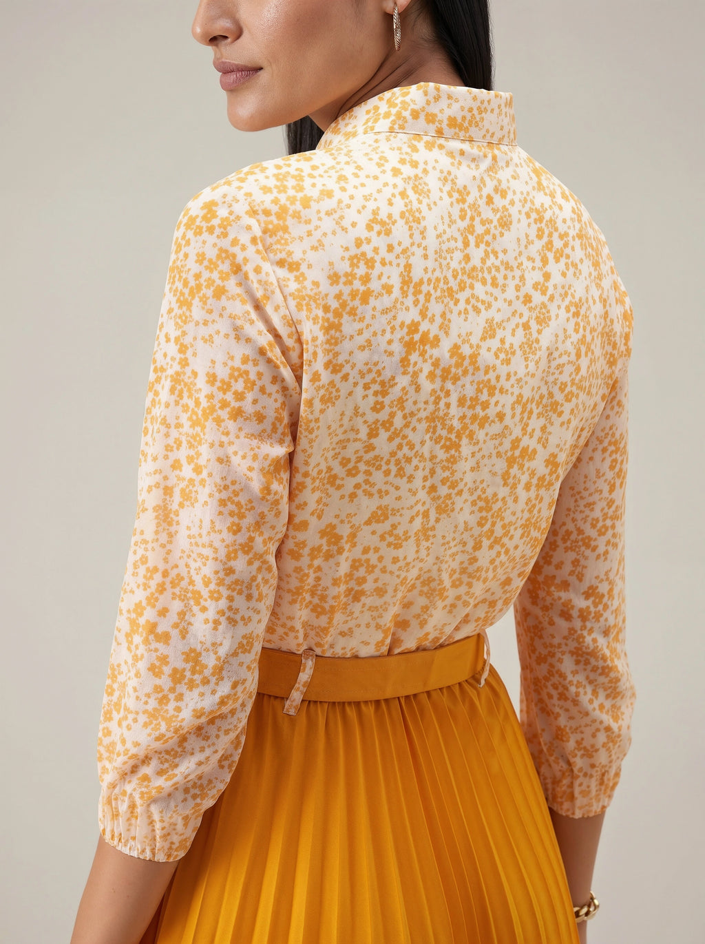 Woman wearing a yellow floral blouse and pleated skirt against a neutral background