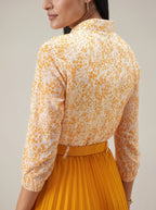Woman wearing a yellow floral blouse and pleated skirt against a neutral background