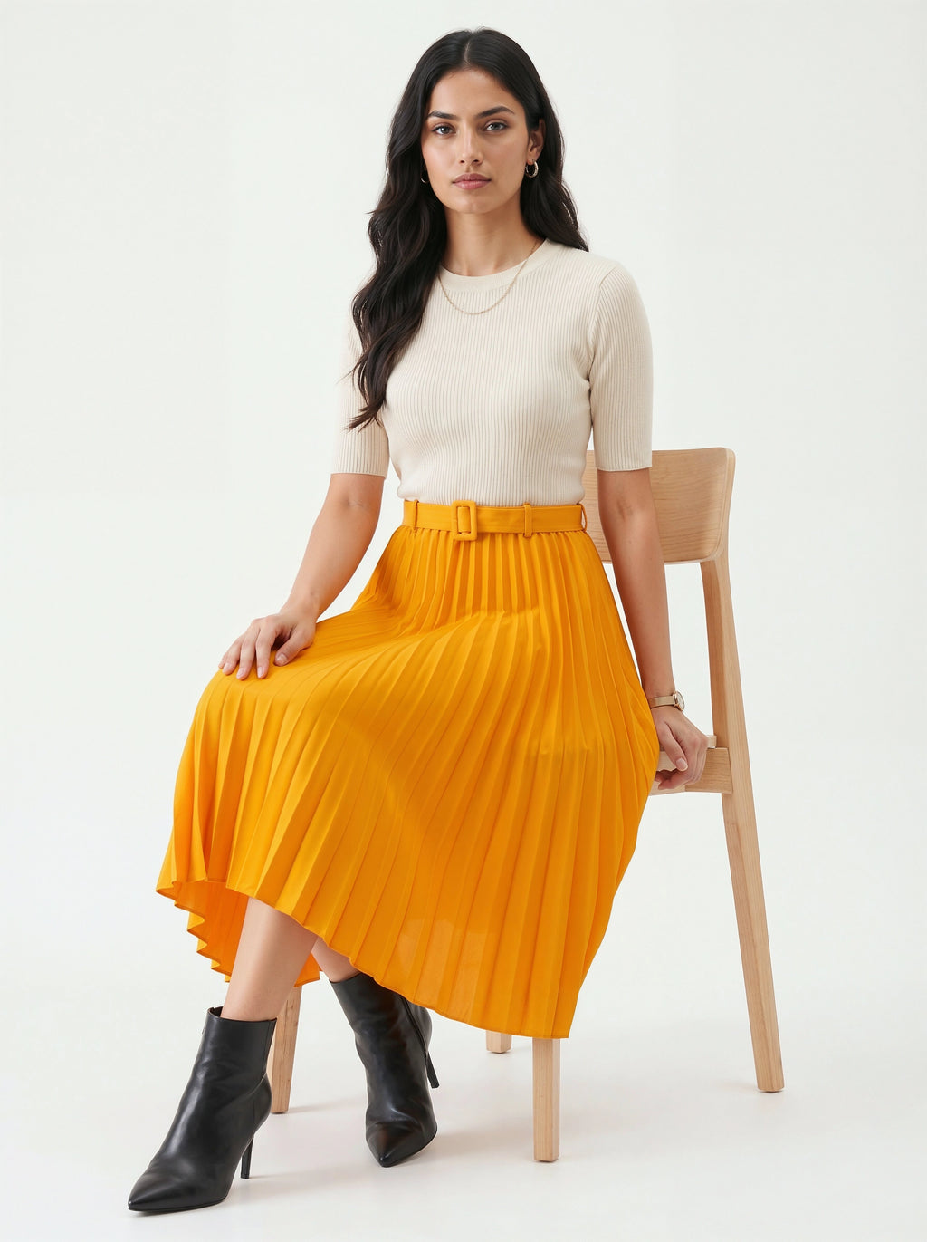 Woman wearing a white top and bright orange skirt sitting on a wooden chair against a white background