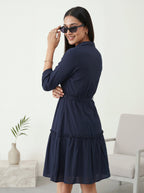Woman wearing a navy blue dress in a minimalistic room.