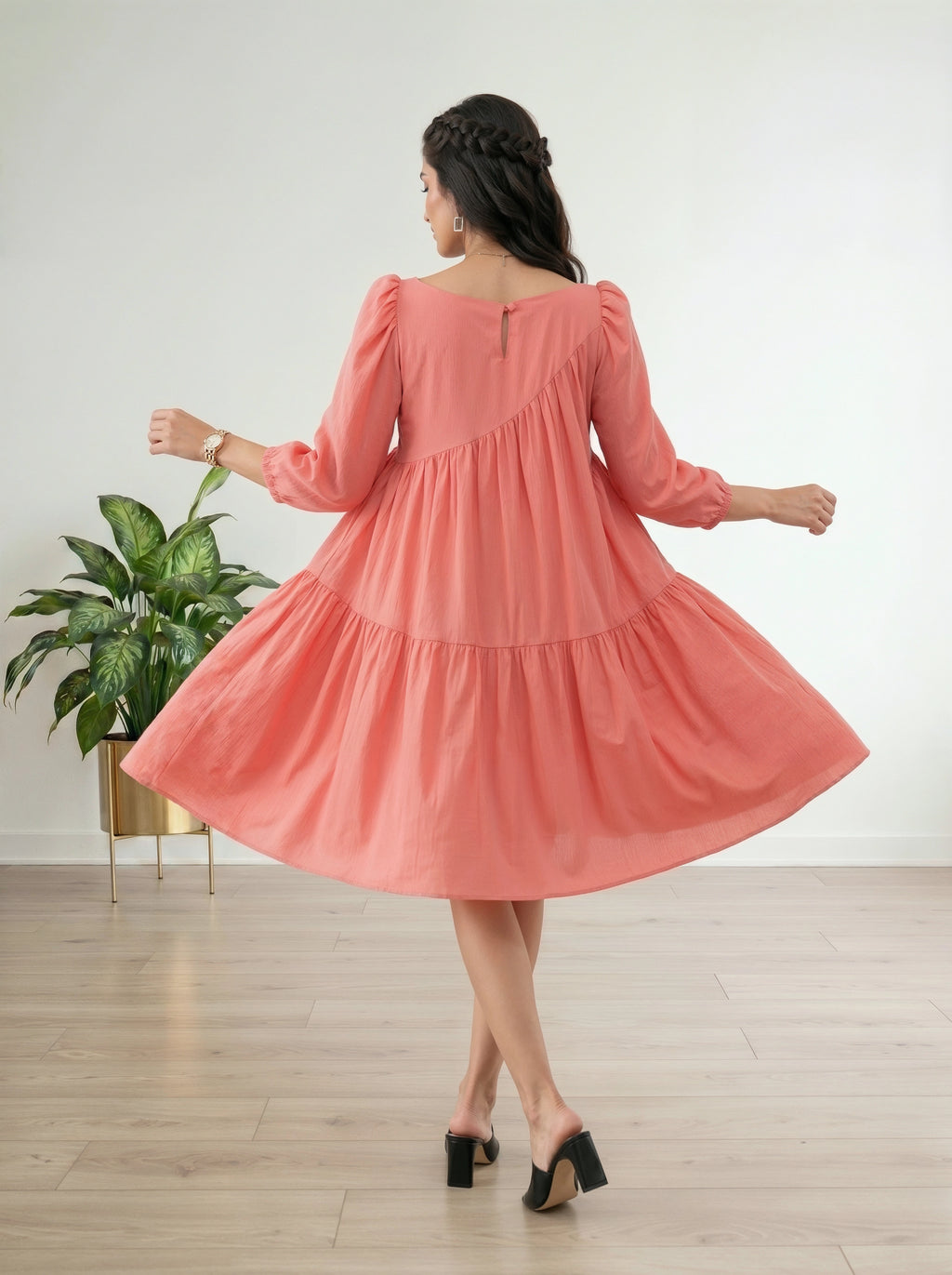 Woman wearing a pink dress in a room with a plant and wooden floor.