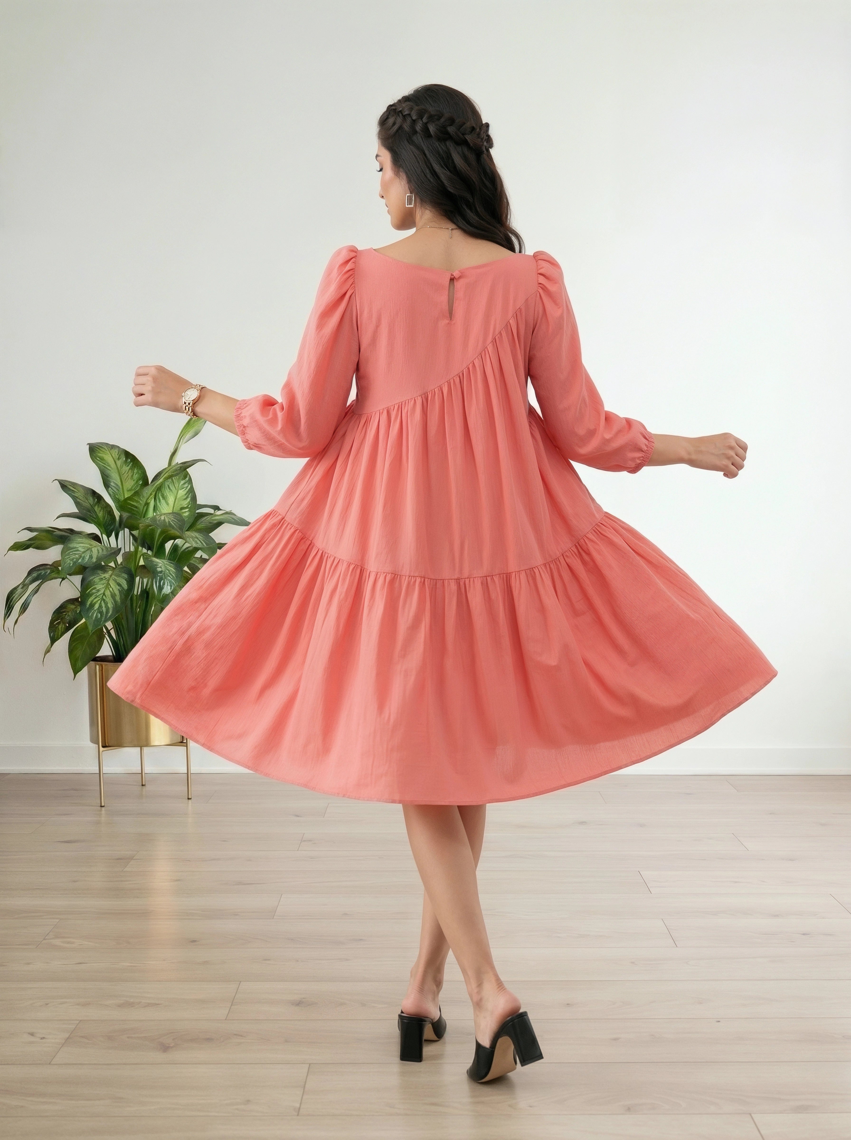 Woman wearing a pink dress in a room with a plant and wooden floor.